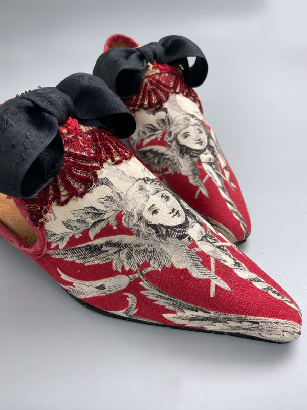 Red, black and white pointed toe bohemian shoes or slippers with a neo-classical winged god motif. Large black silk ribbon bows. Created from antique textiles by Pavilion Parade