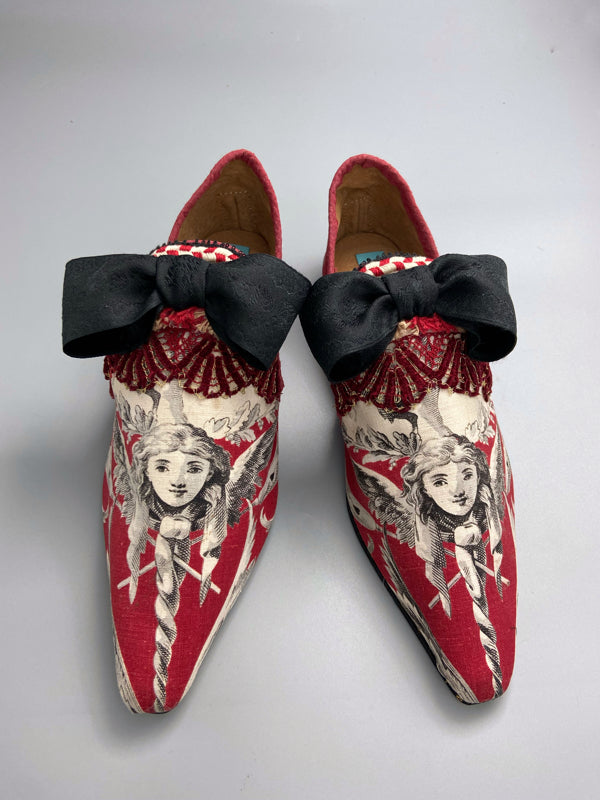 Red, black and white pointed toe bohemian shoes or slippers with a neo-classical winged god motif. Large black silk ribbon bows. Created from antique textiles by Pavilion Parade