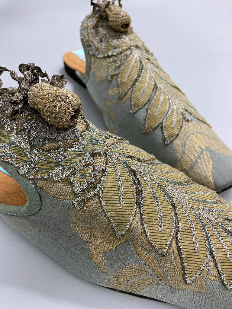 French grey silk brocade and 19th century metallic silver lace are used to create bohemian style shoes with hand worked antique acorn embellishment. Unique style by the Pavilion Parade studio.