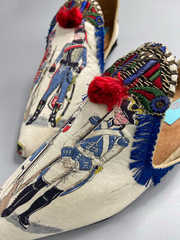 Historic military uniformed soldiers from a vintage French printed toile, and royal bue fringe with scarlet soutache pompom tassels are used to create unique bohemian shoes by Pavilion Parade