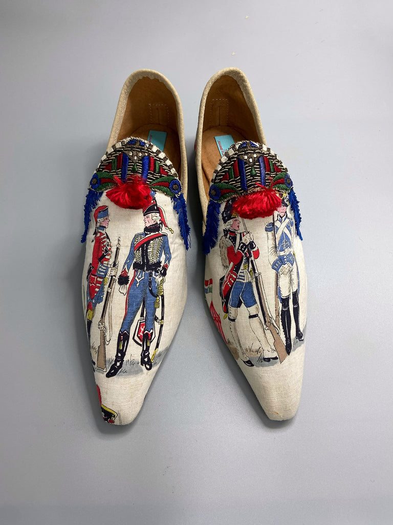 Historic military uniformed soldiers from a vintage French printed toile, and royal bue fringe with scarlet soutache pompom tassels are used to create unique bohemian shoes by Pavilion Parade