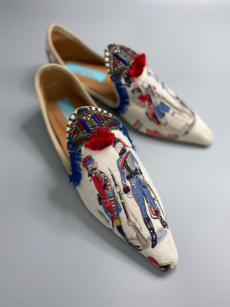 Historic military uniformed soldiers from a vintage French printed toile, and royal bue fringe with scarlet soutache pompom tassels are used to create unique bohemian shoes by Pavilion Parade