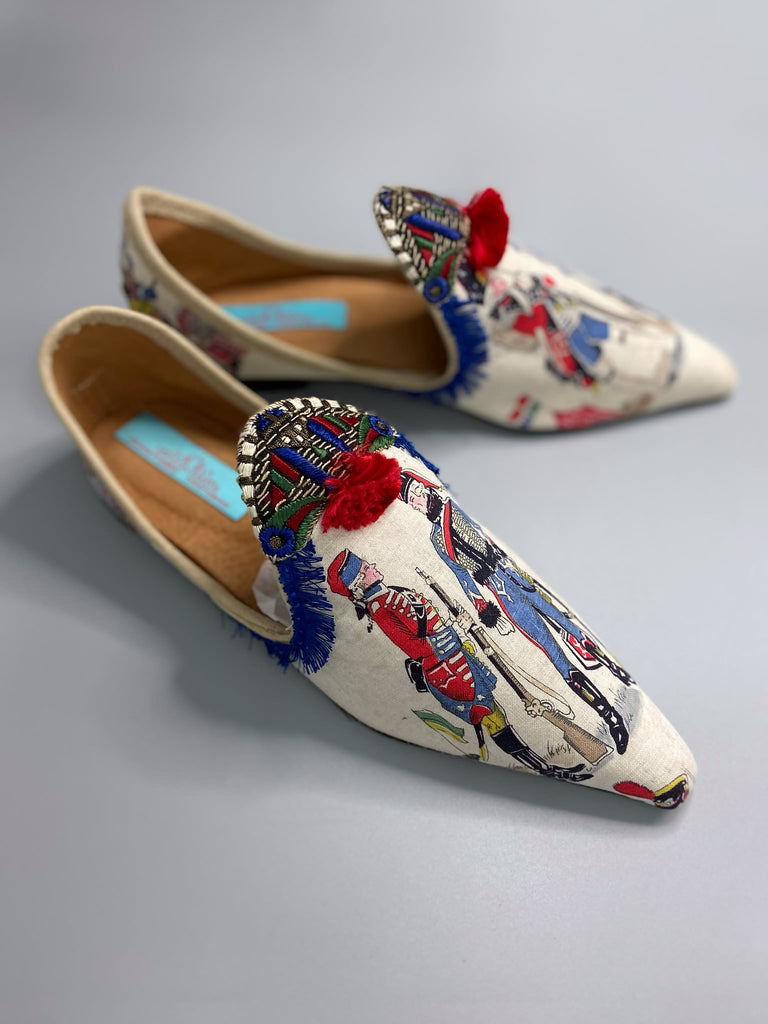 Historic military uniformed soldiers from a vintage French printed toile, and royal bue fringe with scarlet soutache pompom tassels are used to create unique bohemian shoes by Pavilion Parade