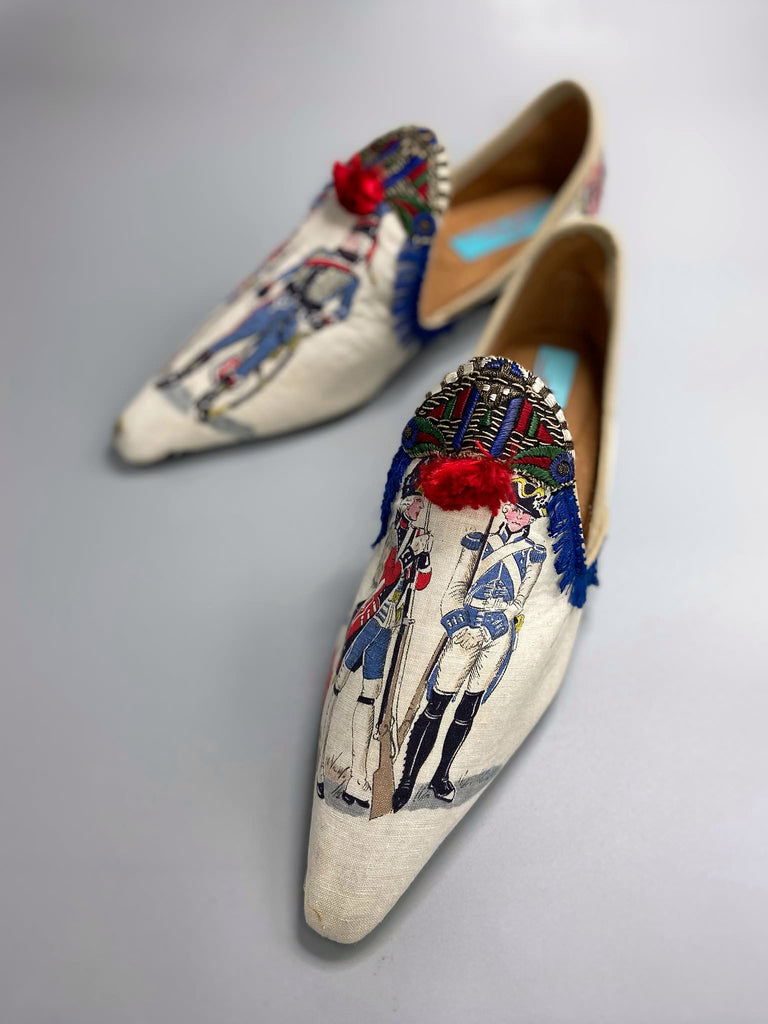 Historic military uniformed soldiers from a vintage French printed toile, and royal bue fringe with scarlet soutache pompom tassels are used to create unique bohemian shoes by Pavilion Parade