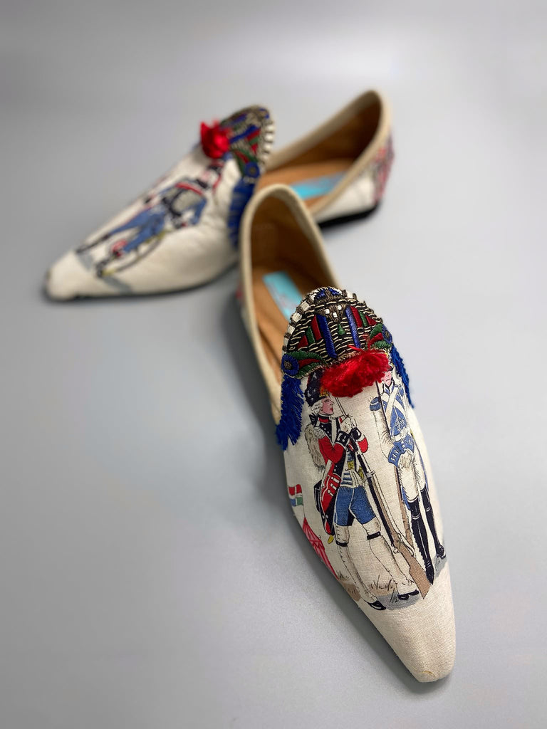 Historic military uniformed soldiers from a vintage French printed toile, and royal bue fringe with scarlet soutache pompom tassels are used to create unique bohemian shoes by Pavilion Parade