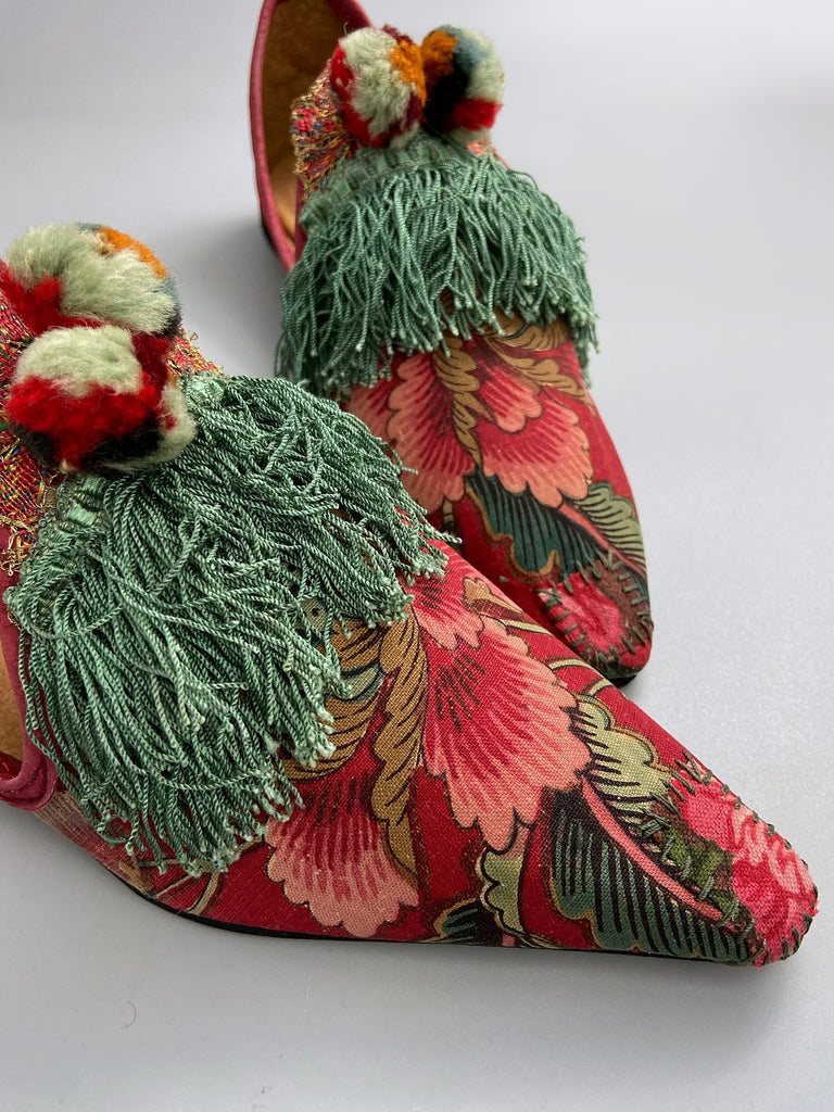 Vibrant floral Indienne toile pointed toe shoes in shades of red pink and green. Embellished with silk tassel fringe, metallic 1920s braid and antique wool pom pom tassels. Bohemian styles sustainably created from antique textiles by the Pavilion Parade studio.