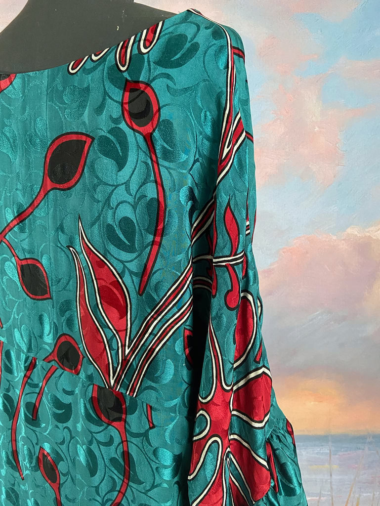 Relaxed fit silk crepe shift dress with full gathered long sleeves, scoop neck and pockets. Teal green with a bold print in black, red, and white. Sustainably created from vintage and antique textiles by the Pavilion Parade studio.