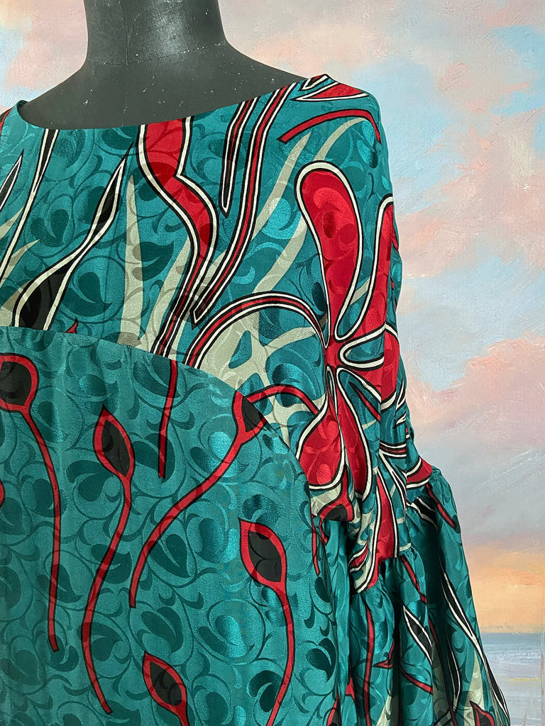 Relaxed fit silk crepe shift dress with full gathered long sleeves, scoop neck and pockets. Teal green with a bold print in black, red, and white. Sustainably created from vintage and antique textiles by the Pavilion Parade studio.