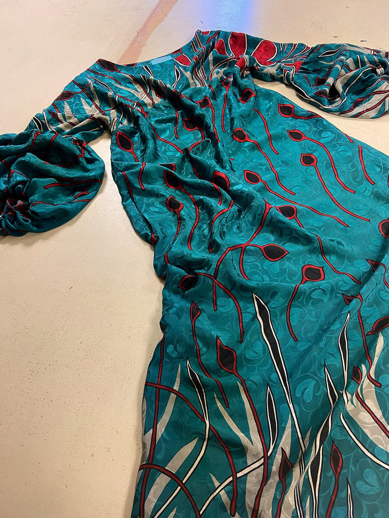 Relaxed fit silk crepe shift dress with full gathered long sleeves, scoop neck and pockets. Teal green with a bold print in black, red, and white. Sustainably created from vintage and antique textiles by the Pavilion Parade studio.