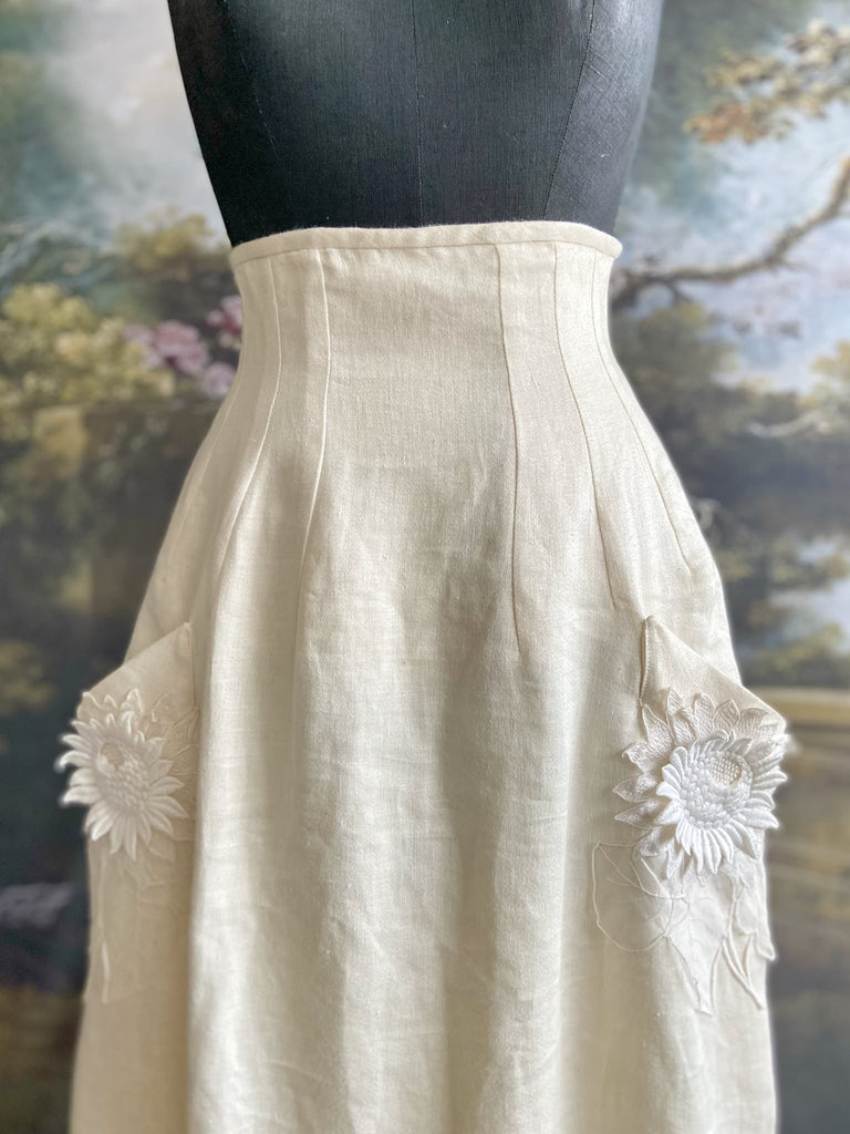 Ivory linen Edwardian style high waisted long skirt with high waist and antique embroidered sunflower appliqués on the deep pockets. Bohemian style from Pavilion Parade.