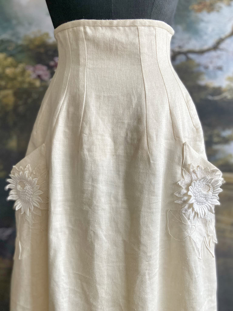 Ivory linen Edwardian style high waisted long skirt with high waist and antique embroidered sunflower appliqués on the deep pockets. Bohemian style from Pavilion Parade.