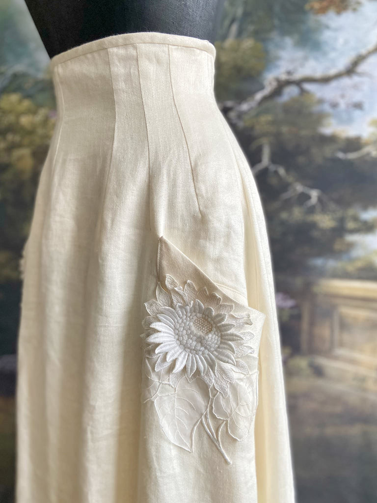 Ivory linen Edwardian style high waisted long skirt with high waist and antique embroidered sunflower appliqués on the deep pockets. Bohemian style from Pavilion Parade.