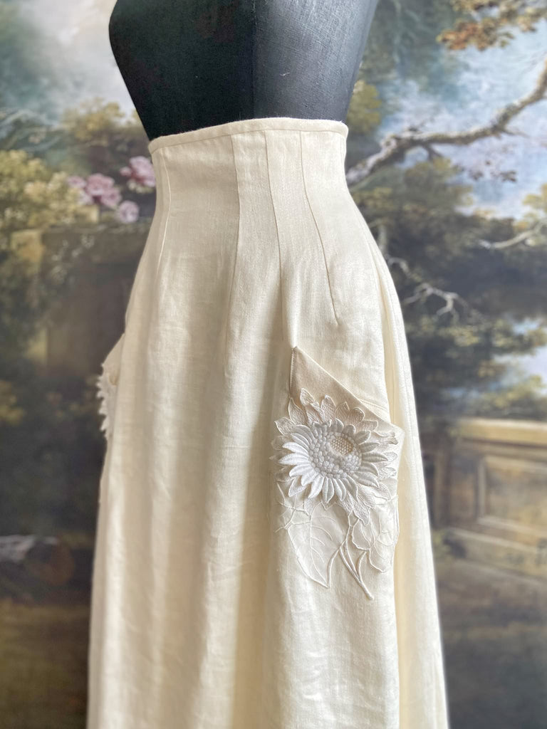 Ivory linen Edwardian style high waisted long skirt with high waist and antique embroidered sunflower appliqués on the deep pockets. Bohemian style from Pavilion Parade.