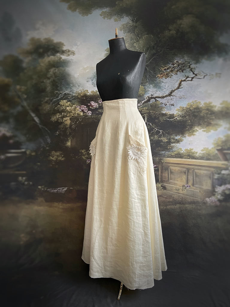 Ivory linen Edwardian style high waisted long skirt with high waist and antique embroidered sunflower appliqués on the deep pockets. Bohemian style from Pavilion Parade.