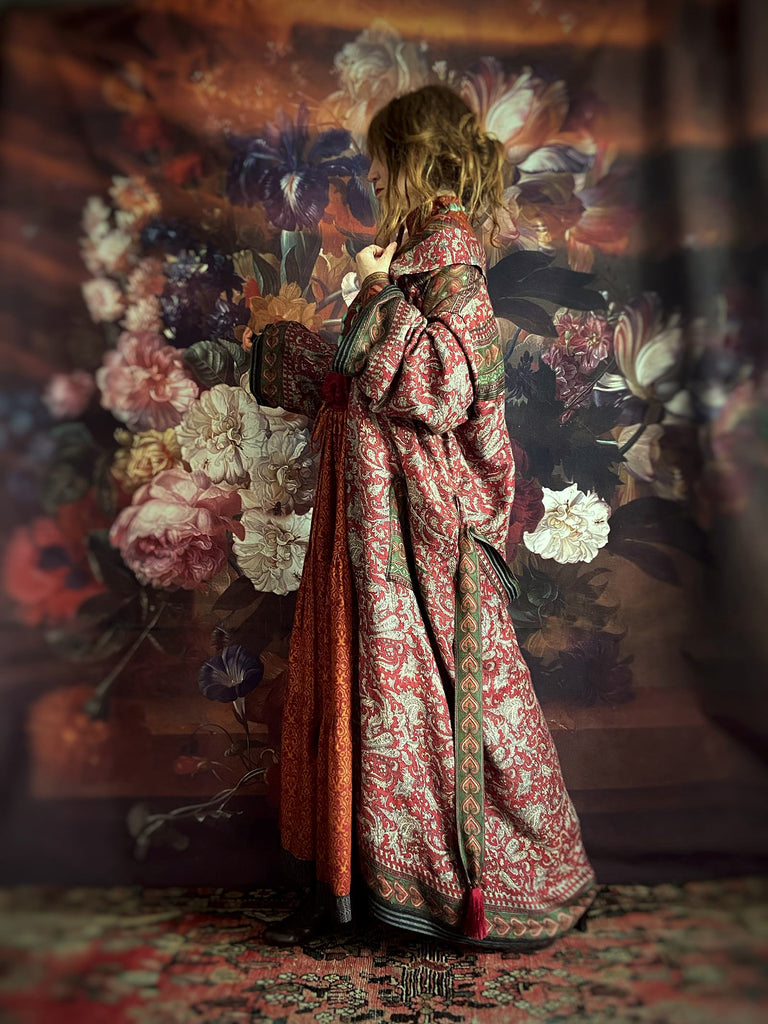 Rusty red fine wool dressing robe created from antique and vintage textiles. A block printed grisaille paisley design, with stylised hearts and geometric border bands at wide cuffs and hem.  Patch pockets and tassel tie belt. Lined in a scrolling floral printed silk. Characterful bohemian garments created in a sustainable fashion by Brighton Bohemian from Pavilion Parade. 