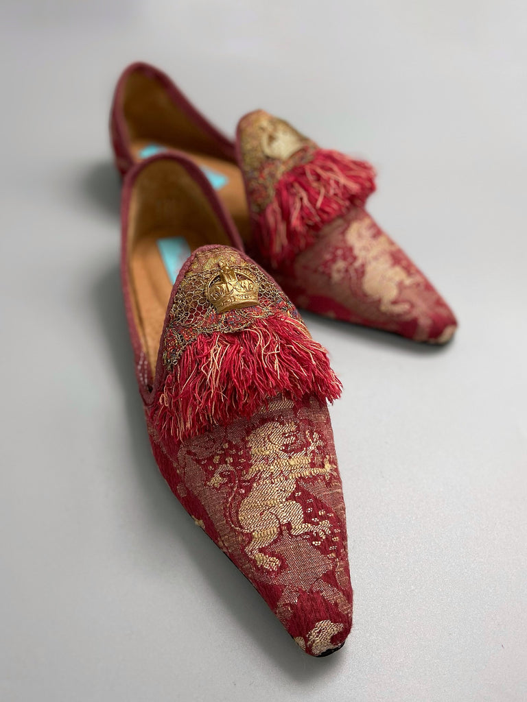 Dark red French brocade slipper shoes with a heraldic design of lions rampant, embellished with early 1800s Florentine silk tassel fringe and aged toleware crowns. Created from antique textiles by Pavilion Parade