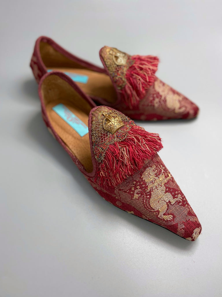 Dark red French brocade slipper shoes with a heraldic design of lions rampant, embellished with early 1800s Florentine silk tassel fringe and aged toleware crowns. Created from antique textiles by Pavilion Parade