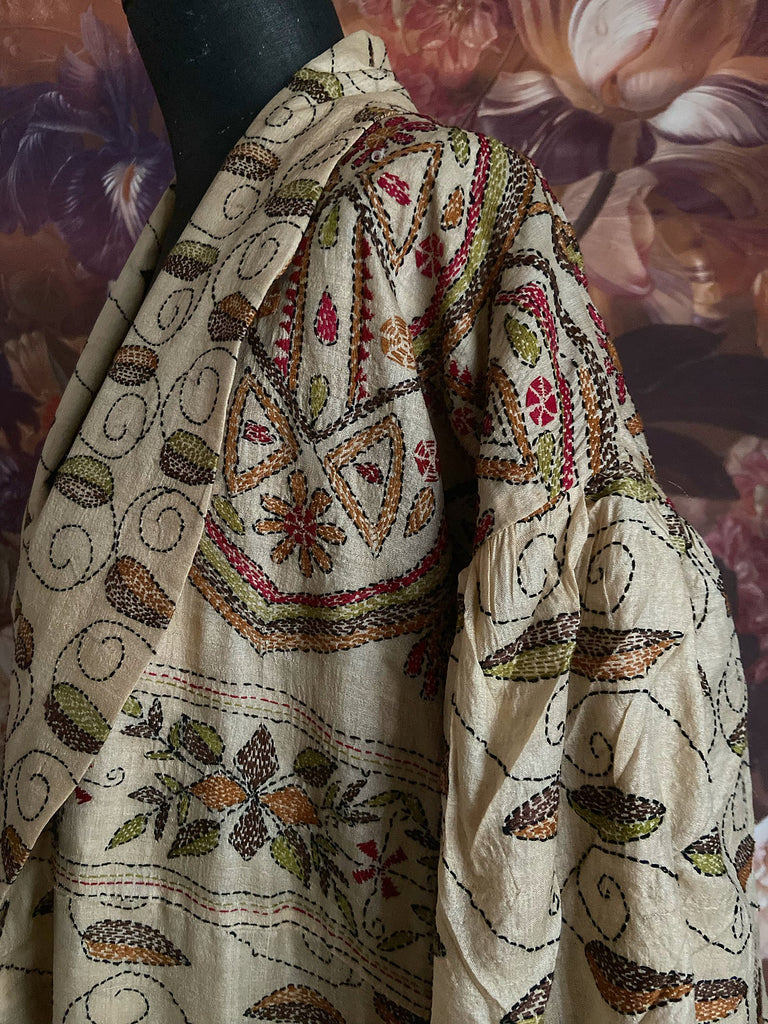 Hand embroidered kantha silk dressing robe or duster coat in an antique ivory shade with leaf green, wine red and chestnut floral embroidery. Wide sleeves, deep pockets and tassel sash belt. Created from vintage and antique textiles by the Pavilion Parade studio.