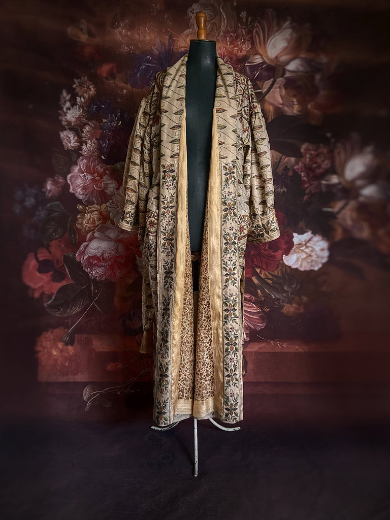 Hand embroidered kantha silk dressing robe or duster coat in an antique ivory shade with leaf green, wine red and chestnut floral embroidery. Wide sleeves, deep pockets and tassel sash belt. Created from vintage and antique textiles by the Pavilion Parade studio.