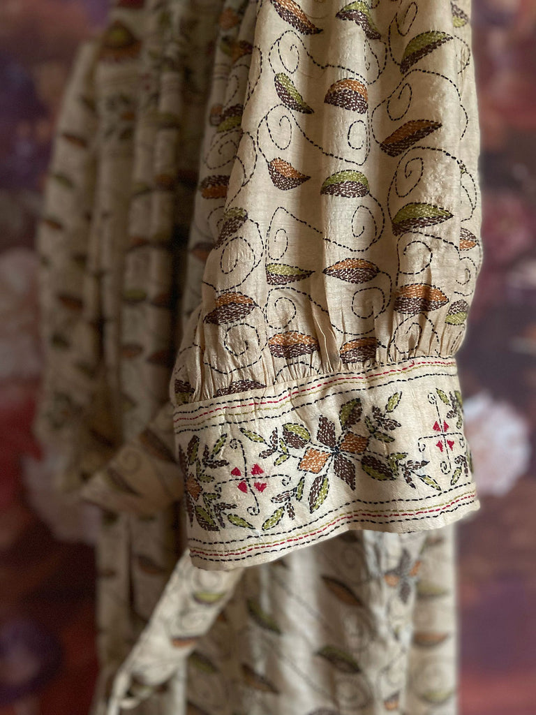 Hand embroidered kantha silk dressing robe or duster coat in an antique ivory shade with leaf green, wine red and chestnut floral embroidery. Wide sleeves, deep pockets and tassel sash belt. Created from vintage and antique textiles by the Pavilion Parade studio.