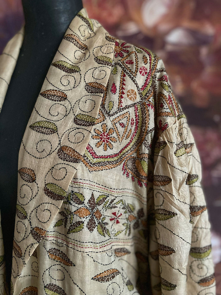 Hand embroidered kantha silk dressing robe or duster coat in an antique ivory shade with leaf green, wine red and chestnut floral embroidery. Wide sleeves, deep pockets and tassel sash belt. Created from vintage and antique textiles by the Pavilion Parade studio.