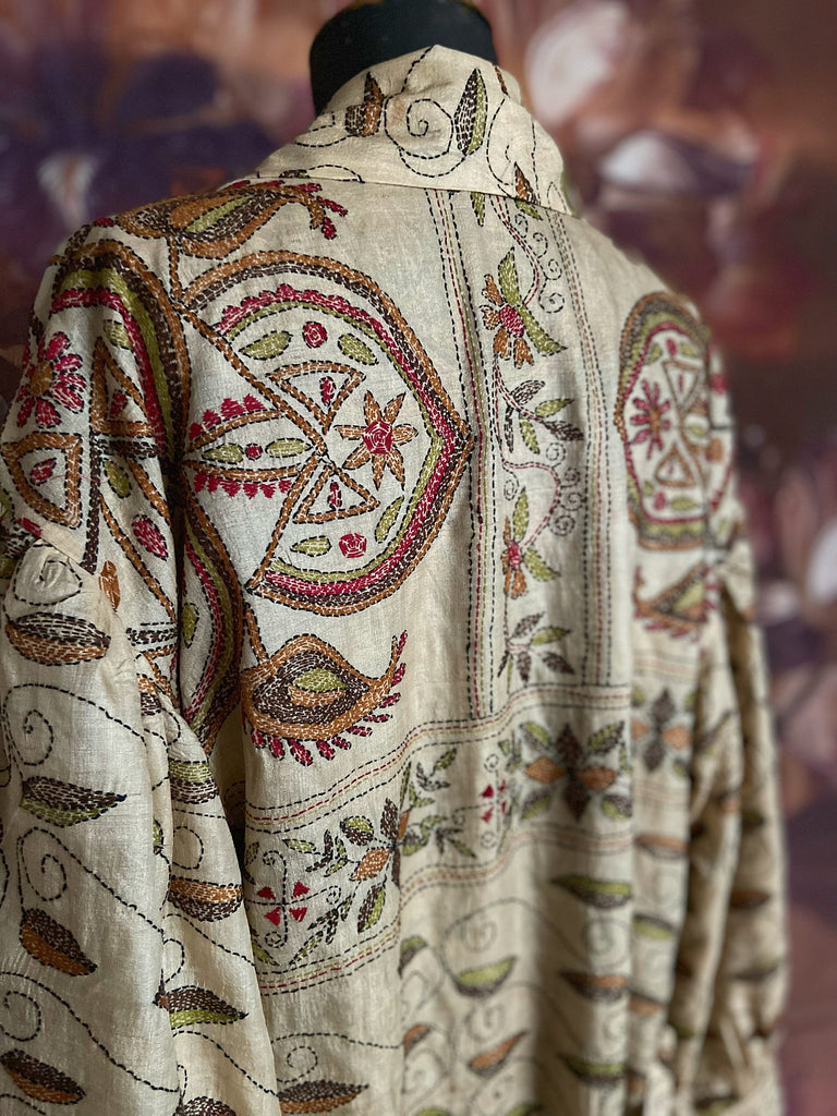Hand embroidered kantha silk dressing robe or duster coat in an antique ivory shade with leaf green, wine red and chestnut floral embroidery. Wide sleeves, deep pockets and tassel sash belt. Created from vintage and antique textiles by the Pavilion Parade studio.