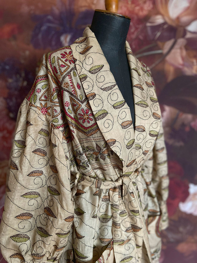 Hand embroidered kantha silk dressing robe or duster coat in an antique ivory shade with leaf green, wine red and chestnut floral embroidery. Wide sleeves, deep pockets and tassel sash belt. Created from vintage and antique textiles by the Pavilion Parade studio.