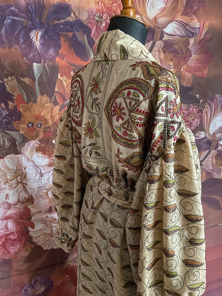 Hand embroidered kantha silk dressing robe or duster coat in an antique ivory shade with leaf green, wine red and chestnut floral embroidery. Wide sleeves, deep pockets and tassel sash belt. Created from vintage and antique textiles by the Pavilion Parade studio.